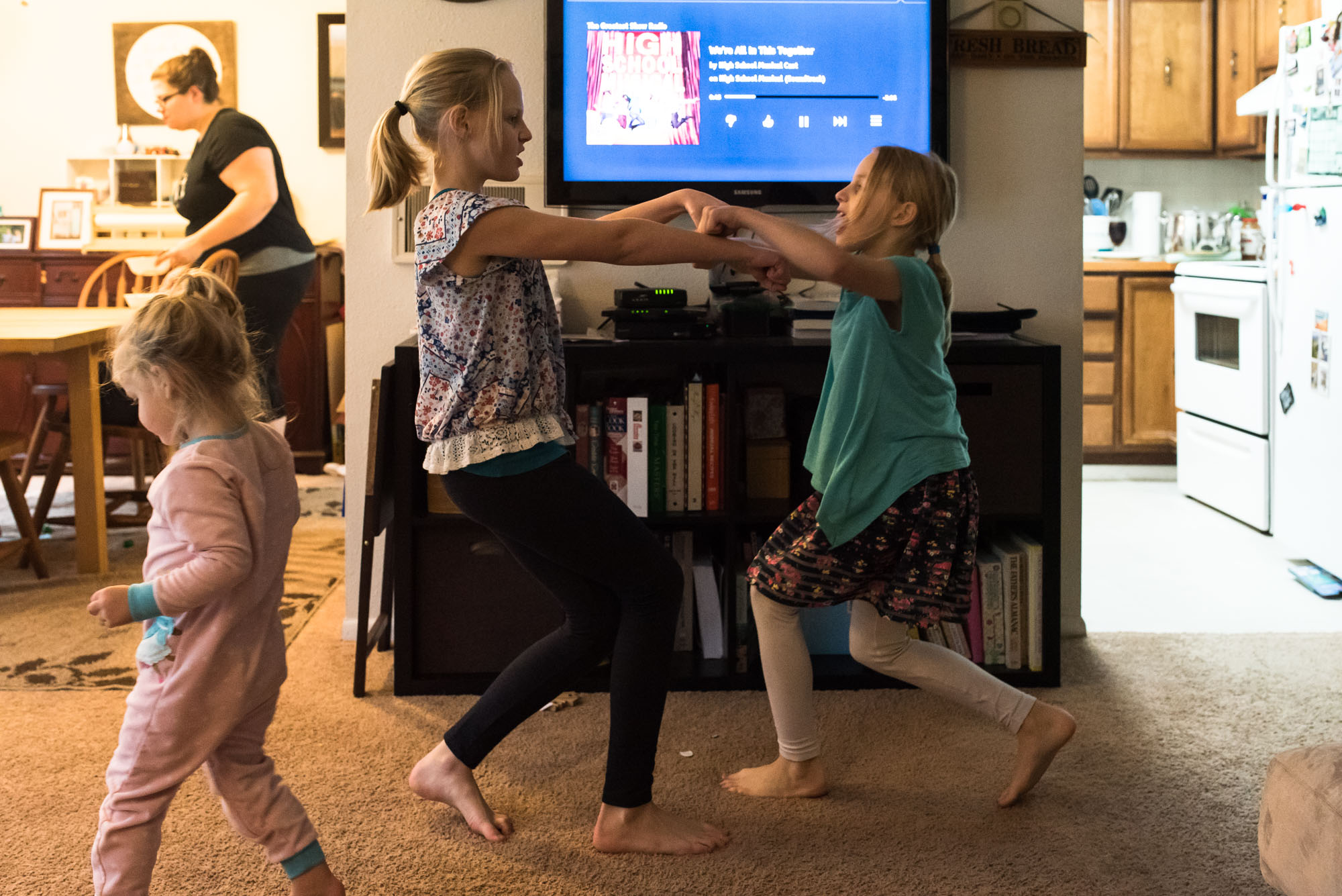 girls dance to music while mom prepares dinner - documentary photography military families