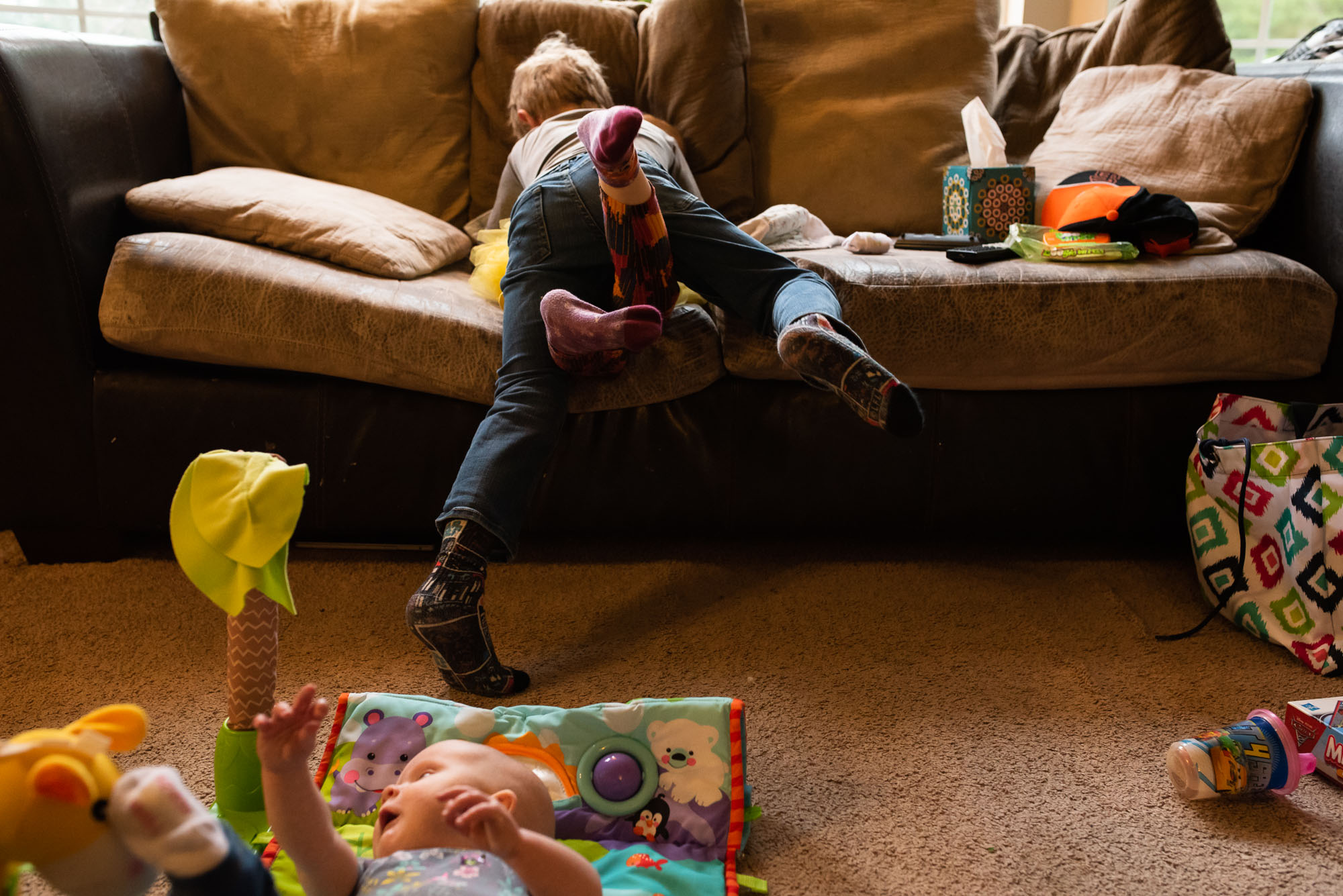 brother and sister rough house while baby lays on floor - documentary photography of military families