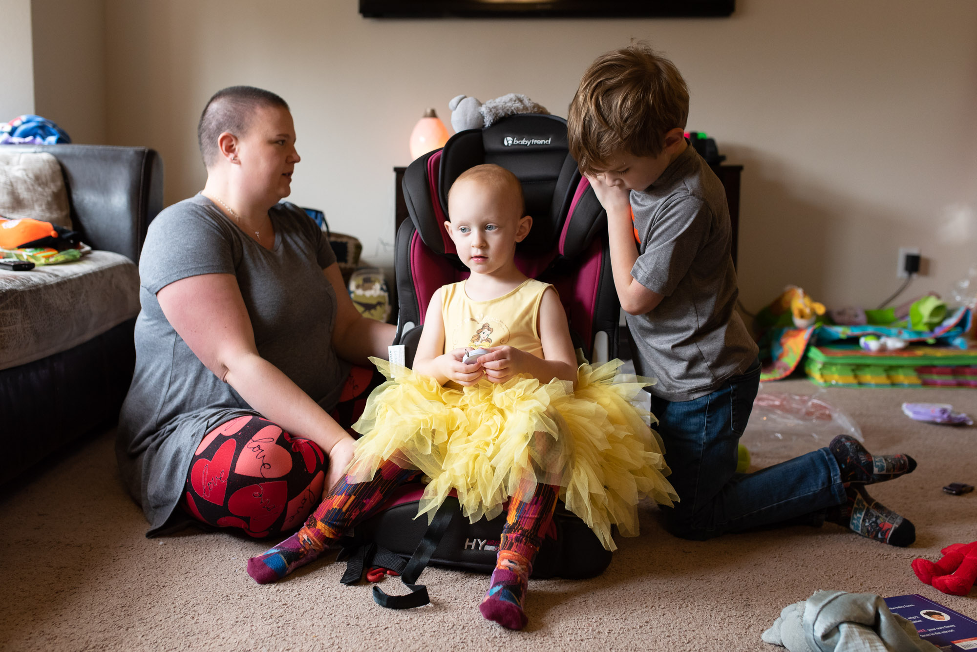 child tests car seat while mother and brother look on - documentary photography of military families