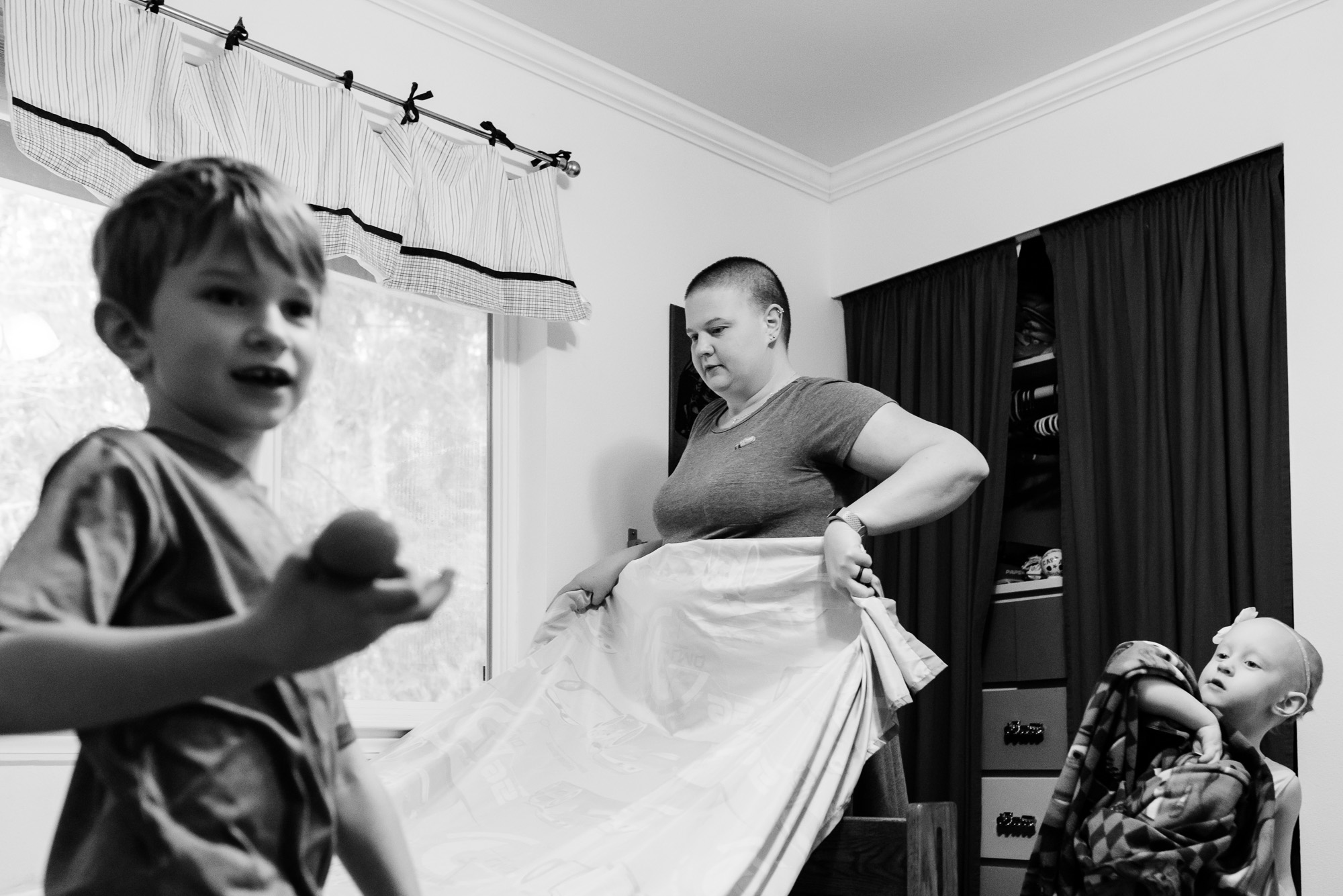 mother makes bed while children are around -documentary photography of military families