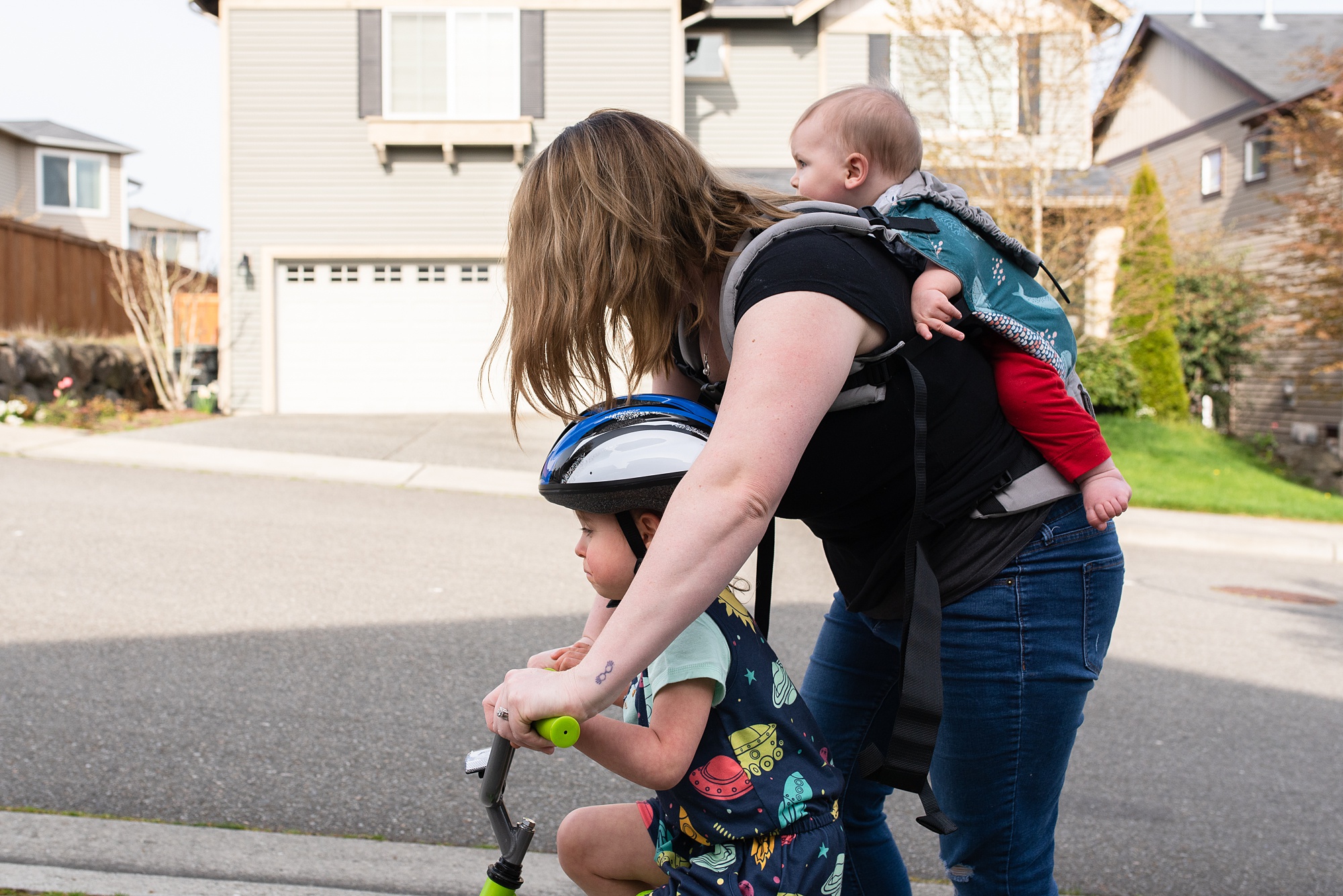 mom assists 3 year old with bike while baby is on back
