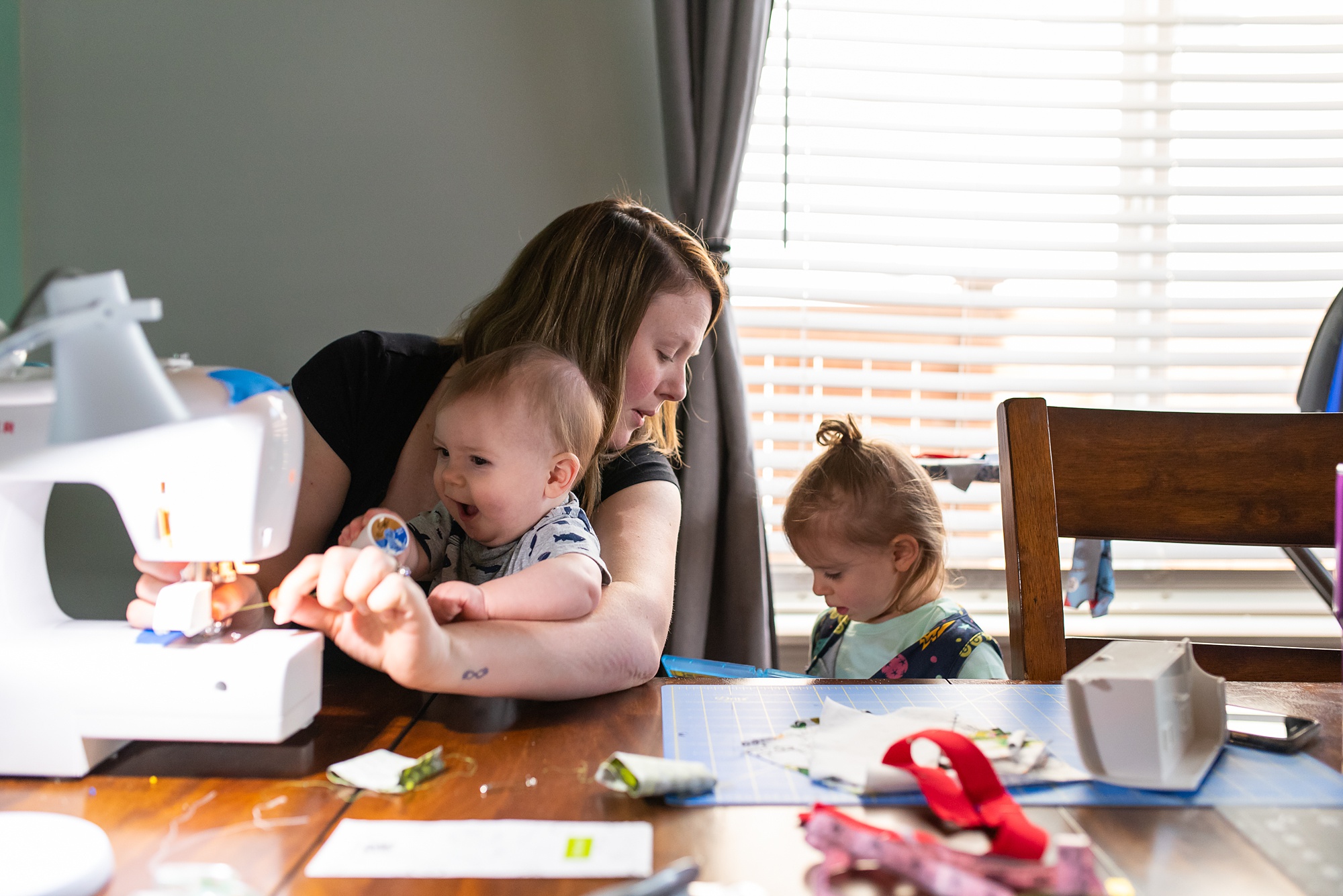 mom sews with baby in lap and talking with daughter