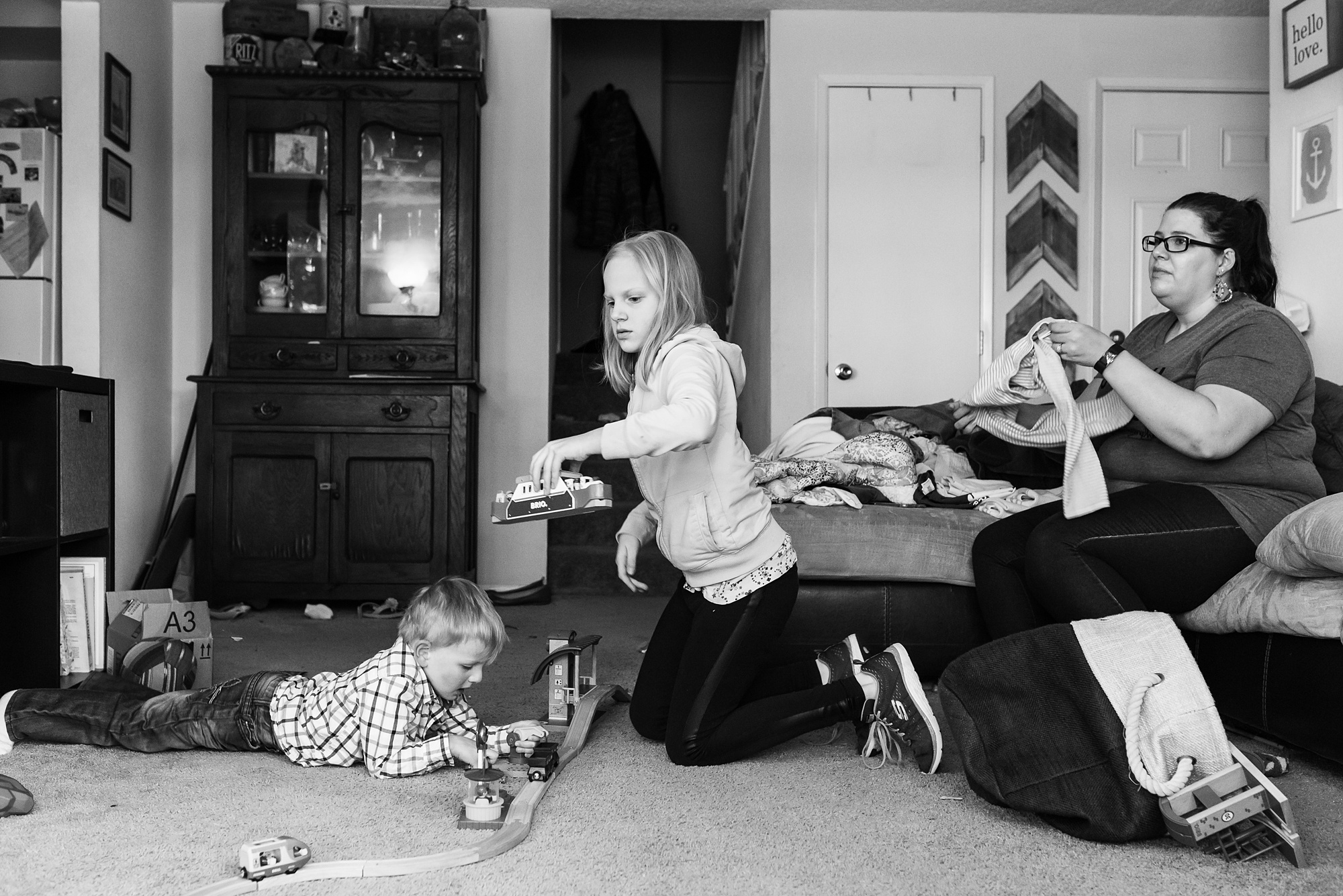 mom folds laundry while kids play trains - military family photography