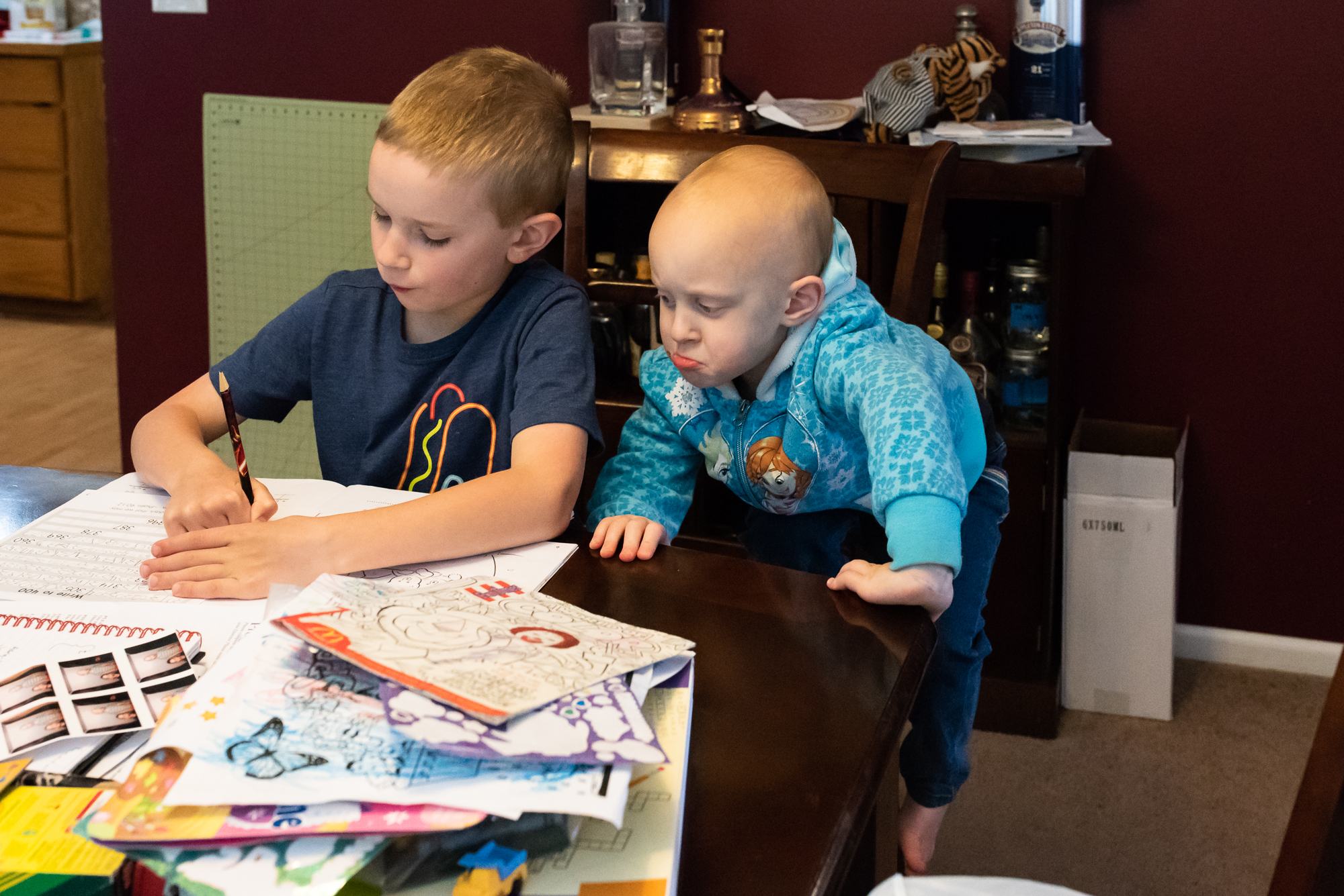 sister looks over brother's shoulder while doing homework