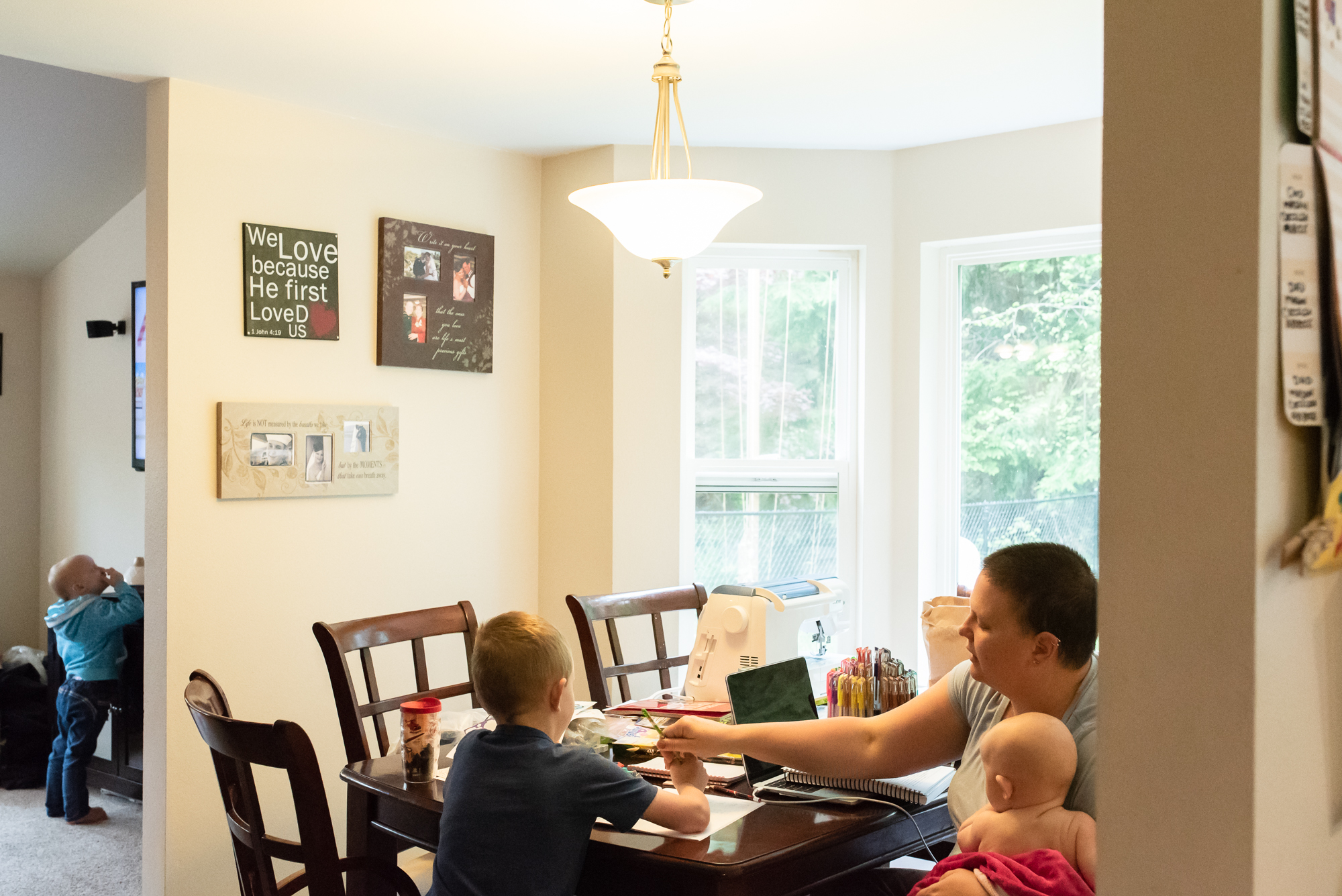 mom does school work with son while girl watches TV in next room